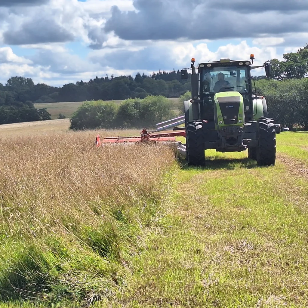 A Chowns Agricultural Services A green tractor driving through a field of tall grass in Worcestershire.