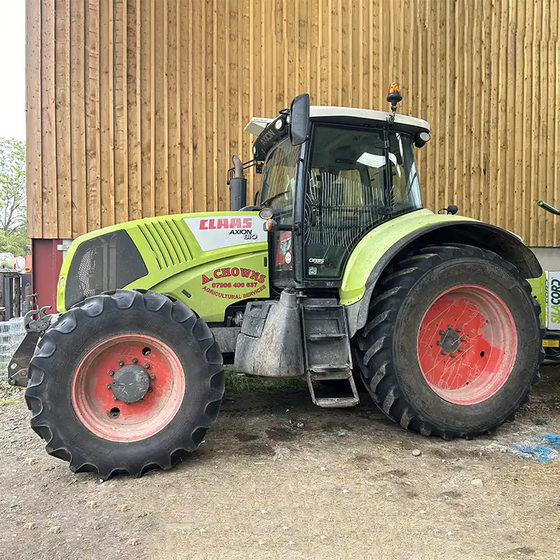 A Chowns Agricultural Services A green tractor parked in front of a barn, representing the importance of farming in Worcestershire.